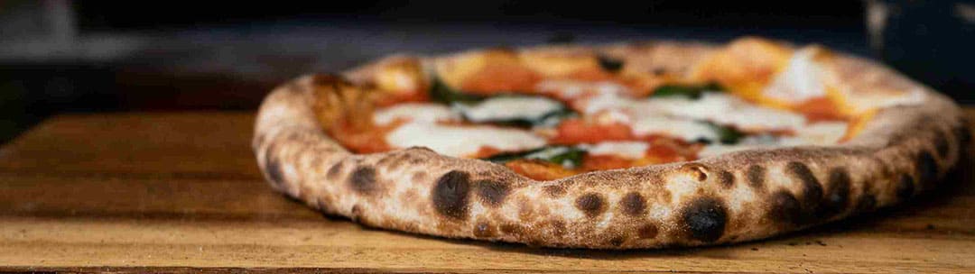 Pizza margherita a la piedra, recién horneada, con el borde tostado y burbujeante